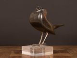 sculpture of a bird sitting on a clear base on a wooden table
