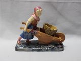 figurine représentant une femme poussant une brouette sur laquelle est posé un panier