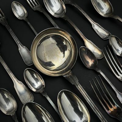 de nombreuses cuillères et fourchettes en argent posées sur une table noire