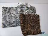 Trois sacs sont alignés sur une surface blanche ; l'un est marron et l'autre est noir et blanc.
