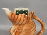 a ceramic teapot shaped like a cat with a green bow tie on its neck