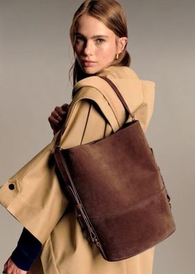 the woman is carrying a brown bag while wearing a tan coat