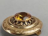 a close up of a gold broochle with a faceted citrine stone