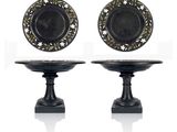 pair of black and gold plates on pedestals on white background