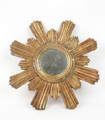 a gold starburst shaped mirror on a white wall
