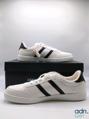 une paire de baskets blanches à rayures noires est posée sur une boîte