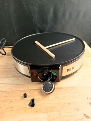 une crêpière posée sur une table en bois, avec un tableau noir en arrière-plan
