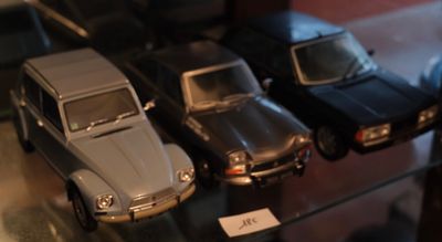 Plusieurs petites voitures sont alignées sur une étagère en verre dans une vitrine.