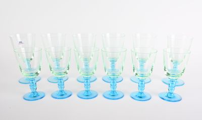 six verres à vin bleus et verts alignés sur une surface blanche
