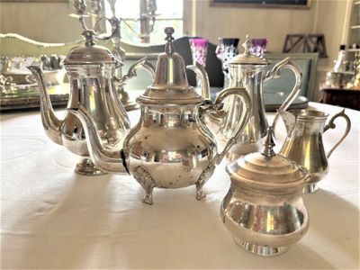 five silver teapots sitting on a table in the middle of a room