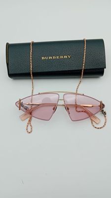 une paire de lunettes de soleil roses avec une chaîne dorée, posée sur un fond blanc