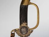 a close up of a sword with a gold handle and a medallion on it