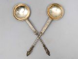 paire de cuillères anciennes en argent avec des manches, posées sur une surface blanche
