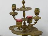 a three - tiered brass candelab with red glass cups on it