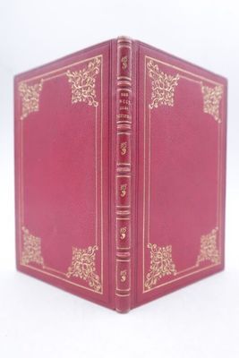 un vieux livre rouge avec des bordures dorées posé sur une surface blanche