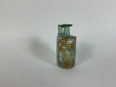 une petite bouteille en verre vert munie d'une anse, posée sur une surface blanche