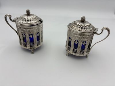 pair of silverplated teapots with blue glass in the shape of a birdcage
