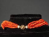 an orange beaded necklace with a gold clasp on a black velvet mannequin