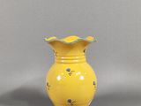 un vase jaune orné de fleurs bleues, posé sur un fond gris