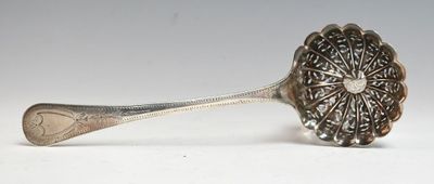 une cuillère en argent ornée d'un motif floral, posée sur une surface blanche