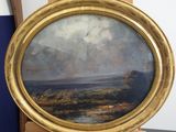 une peinture à l'huile représentant un paysage, dans un cadre doré, posée sur un chevalet en bois