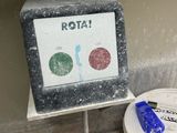 a toilet with a sign that says rota next to a bucket of toilet paper