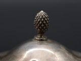 an antique silver teapot with a pine cone on top