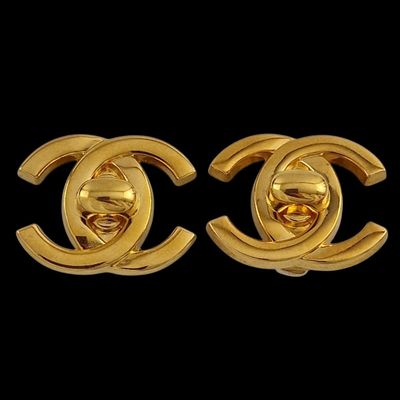 a pair of gold toned chanel earrings on a black background
