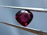 une image représentant un diamant en forme de cœur, de couleur rubis, tenu par une pince à épiler