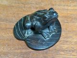 a small bronze frog sitting on a leaf on a wooden table