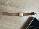 brown leather watch band with gold buckle on a wooden surface