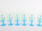 six verres à vin bleus et verts alignés sur une surface blanche