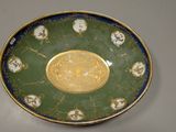 a green and gold plate with a gold medallion on it