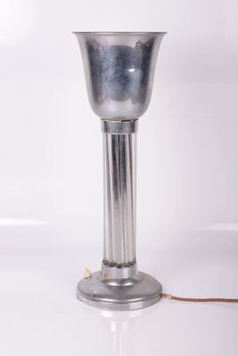 une photo d'une lampe de table en métal argenté posée sur une surface blanche