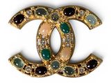 un gros plan d'une broche Chanel ornée de pierres vertes et blanches