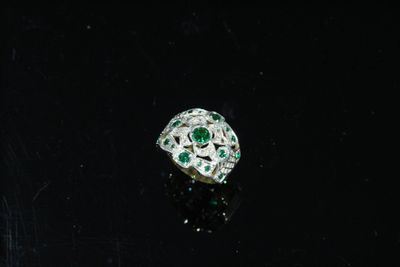 un gros plan d'une bague sertie d'un diamant et d'une émeraude sur une surface noire