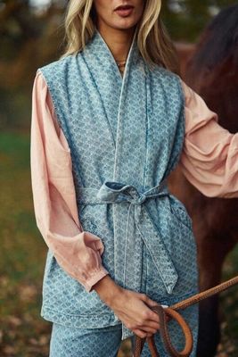 une femme vêtue d'une tenue bleue et rose, debout à côté d'un cheval dans un champ