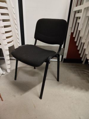 a black chair sitting next to a stack of white chairs