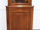 a wooden corner cabinet with a glass door on top of it