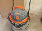 un aspirateur orange et gris posé sur le sol, près d'un mur