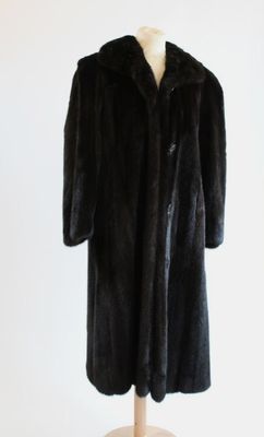 un manteau de fourrure noir posé sur un mannequin, devant un mur blanc