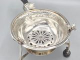 an antique silver plate with a black handle and a metal strainer