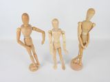 three wooden mannequins standing next to each other on a white surface