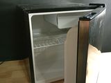 un petit réfrigérateur dont la porte est ouverte, posé sur un plancher en bois