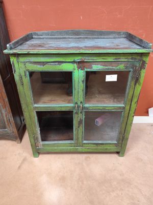 une vieille armoire verte avec des portes vitrées et des étagères, dans une pièce