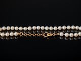 a single strand of pearls with a gold clasp on a black background