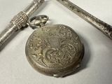a silver pocket watch sitting next to a pair of scissors