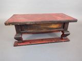 an old wooden table with a red top sitting on a gray surface