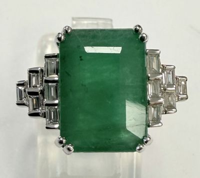 an emerald and diamond ring on display on a white surface