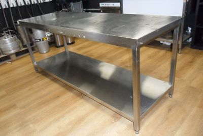 une table en acier inoxydable dans une cuisine, avec des casseroles et des poêles en arrière-plan